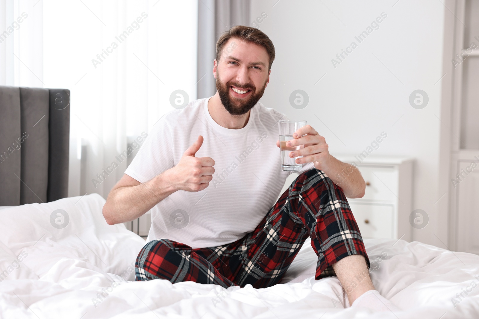 Photo of Happy young man with glass of water near on bed at morning