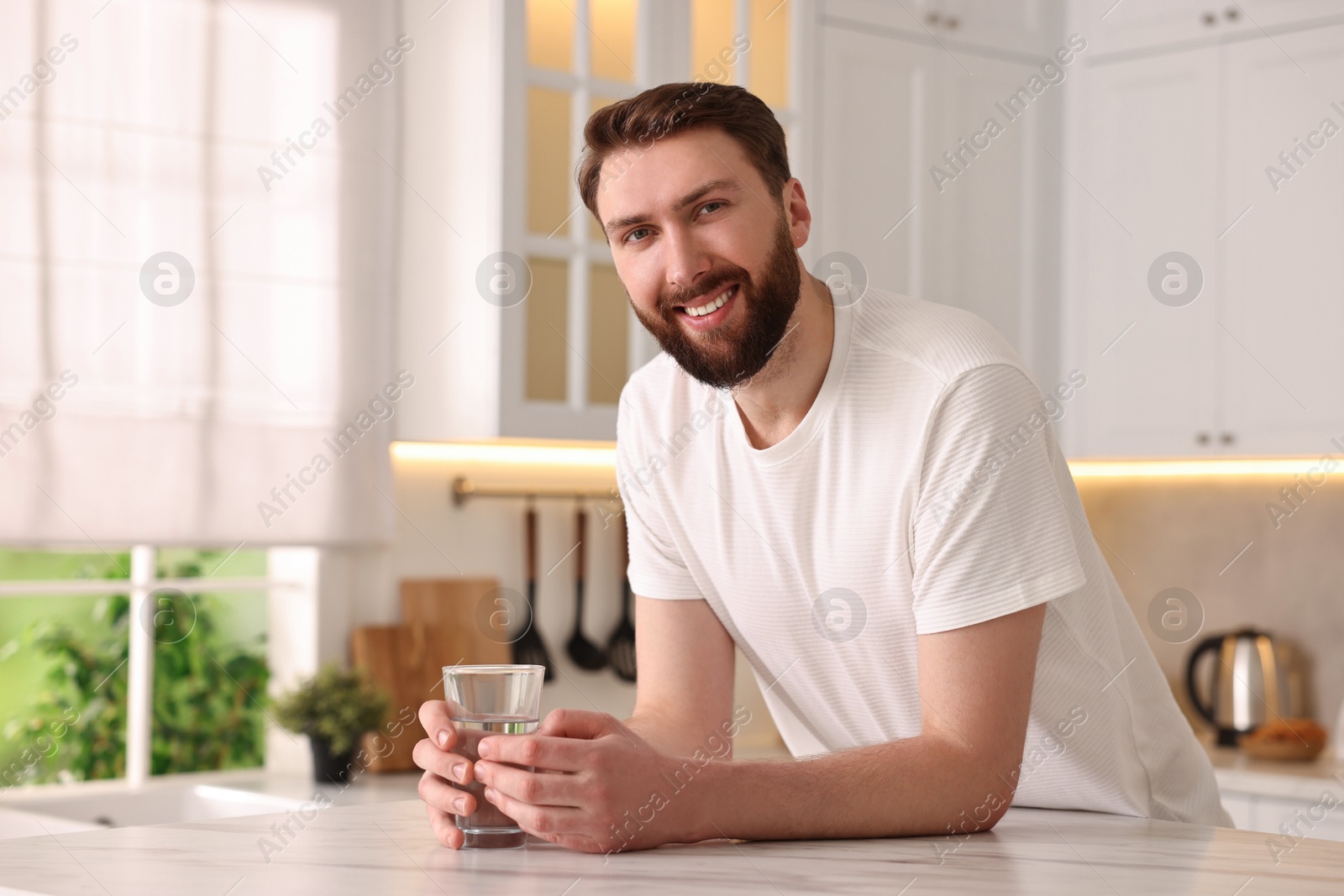 Photo of Happy young man with glass of water in kitchen at morning