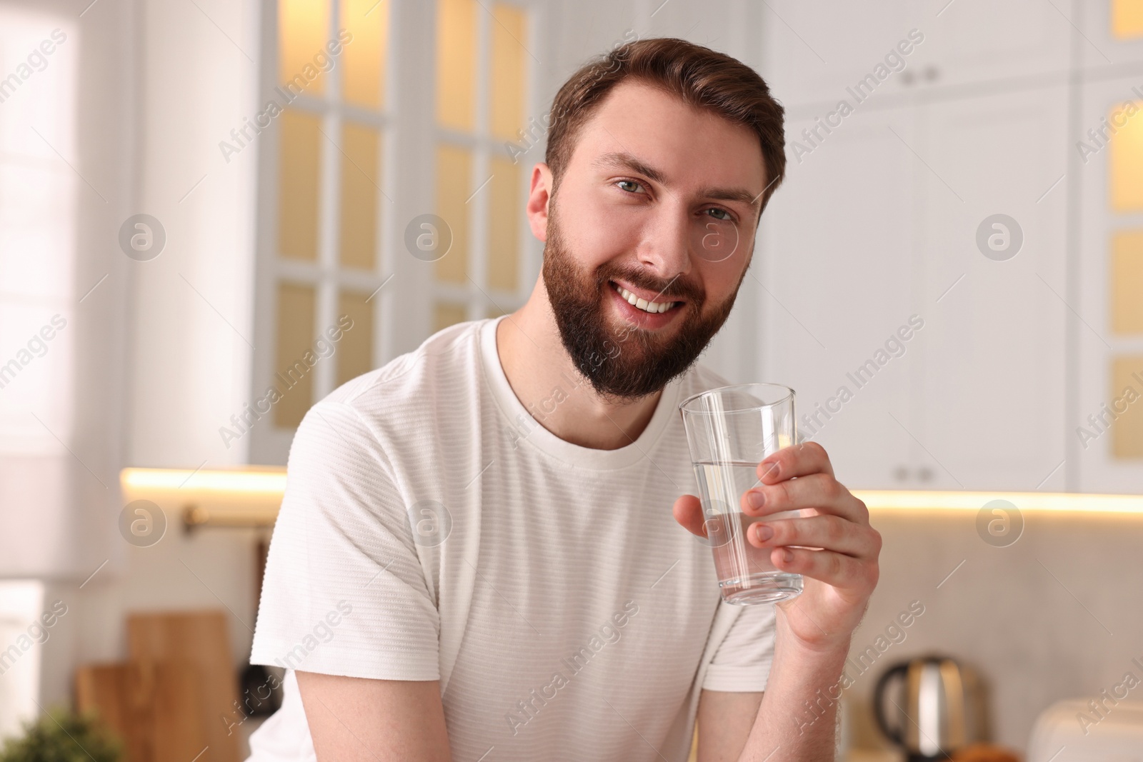 Photo of Happy young man with glass of water in kitchen at morning