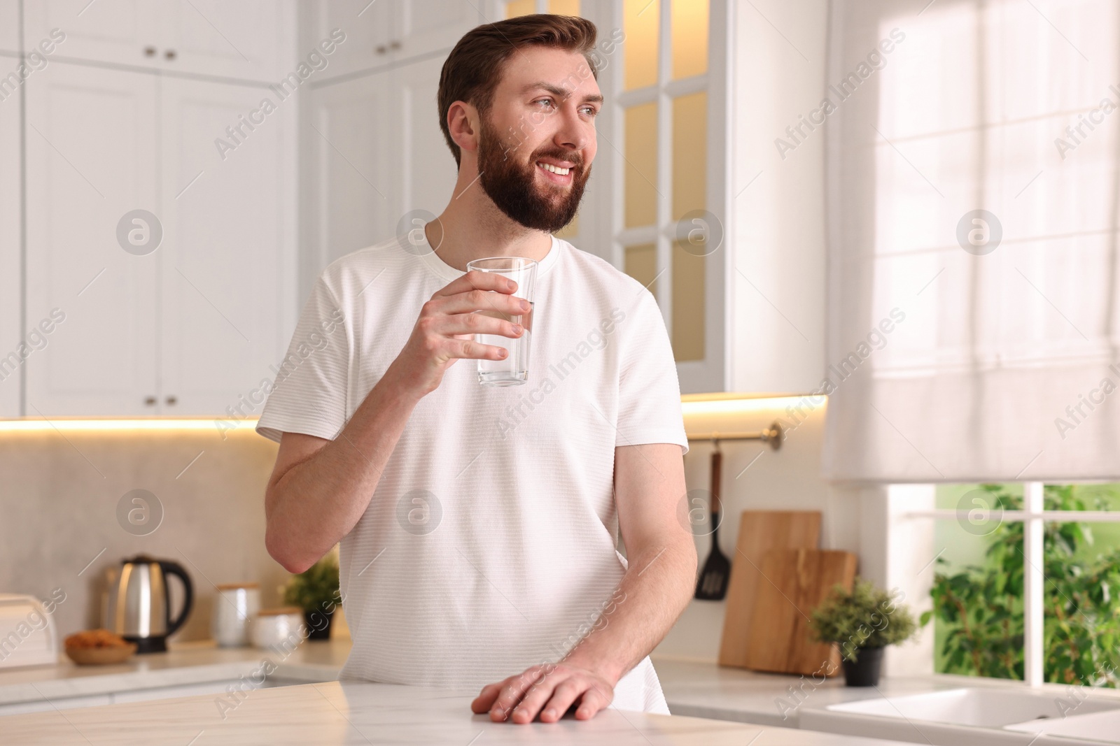 Photo of Happy young man with glass of water in kitchen at morning