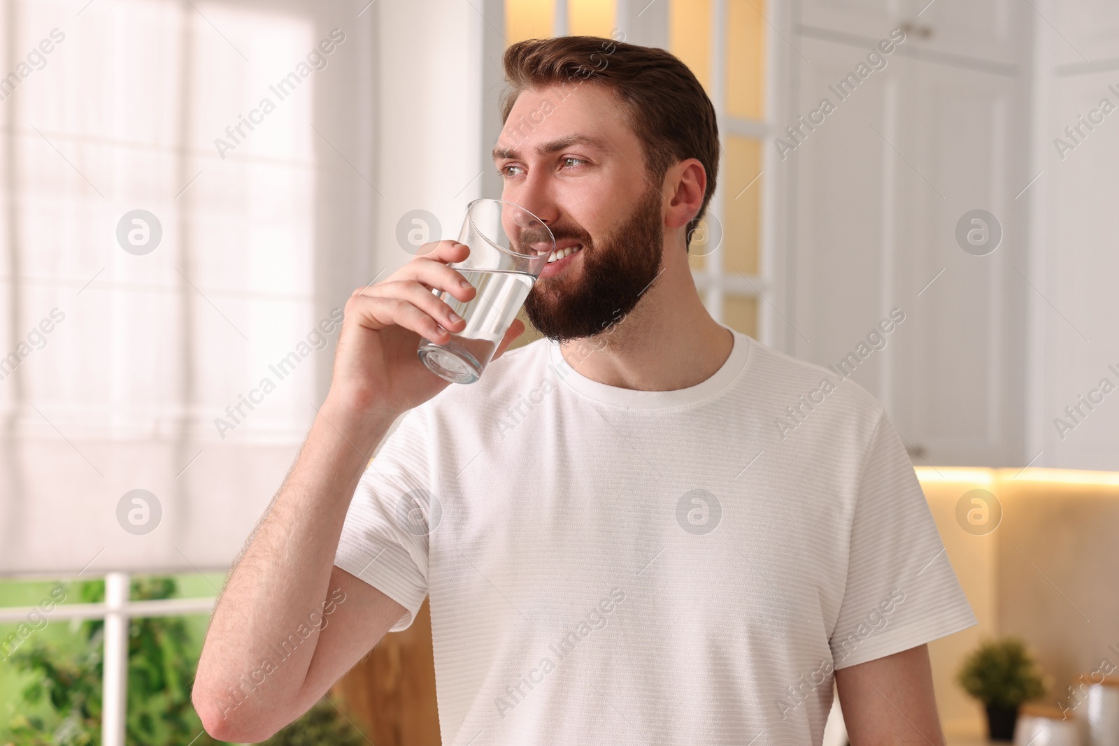 Photo of Happy young man with glass of water in kitchen at morning