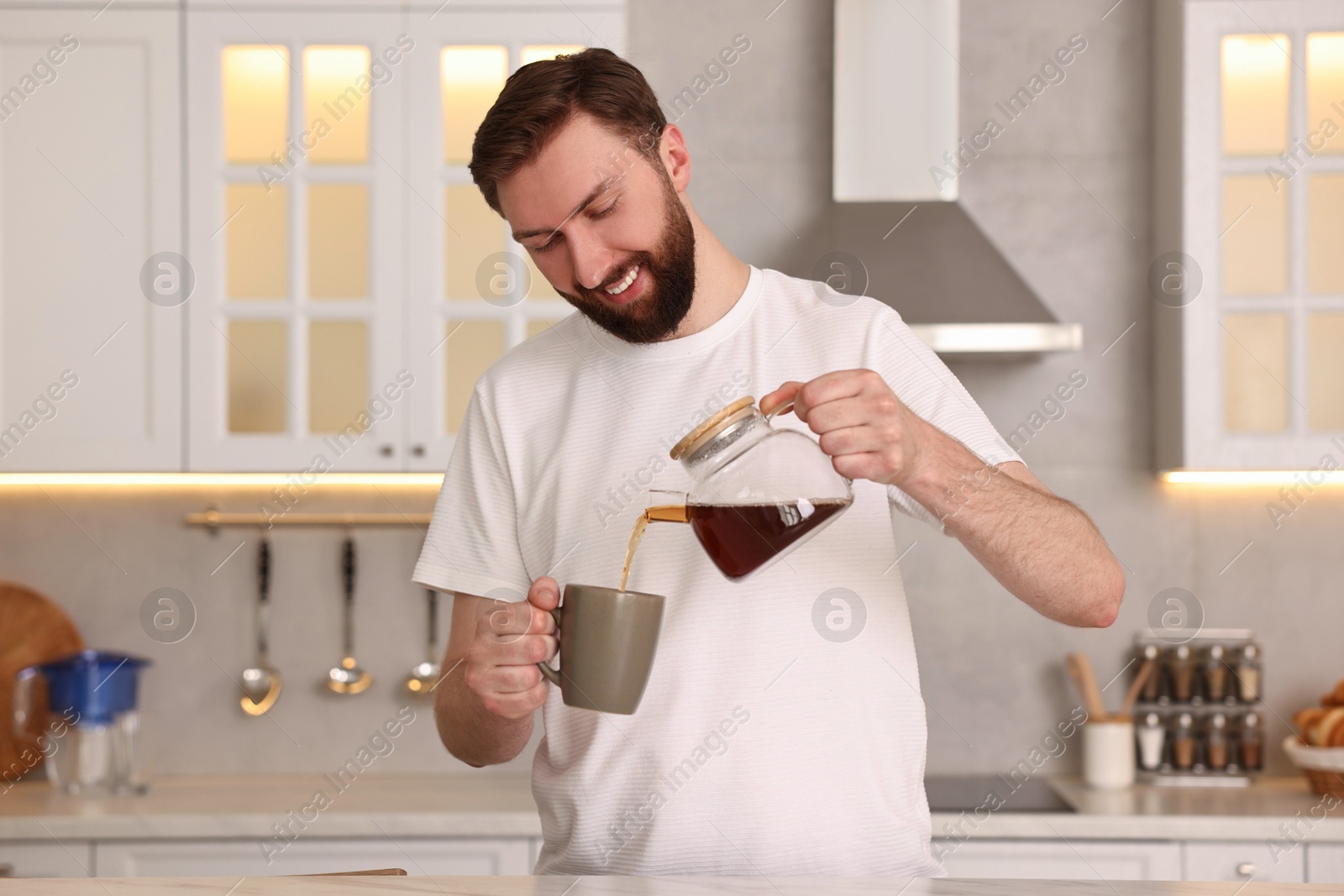 Photo of Happy young man pouring coffee into cup in kitchen at morning