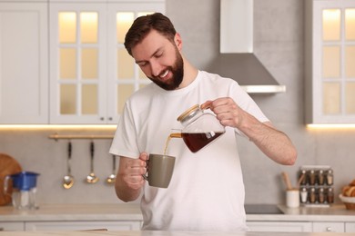 Photo of Happy young man pouring coffee into cup in kitchen at morning