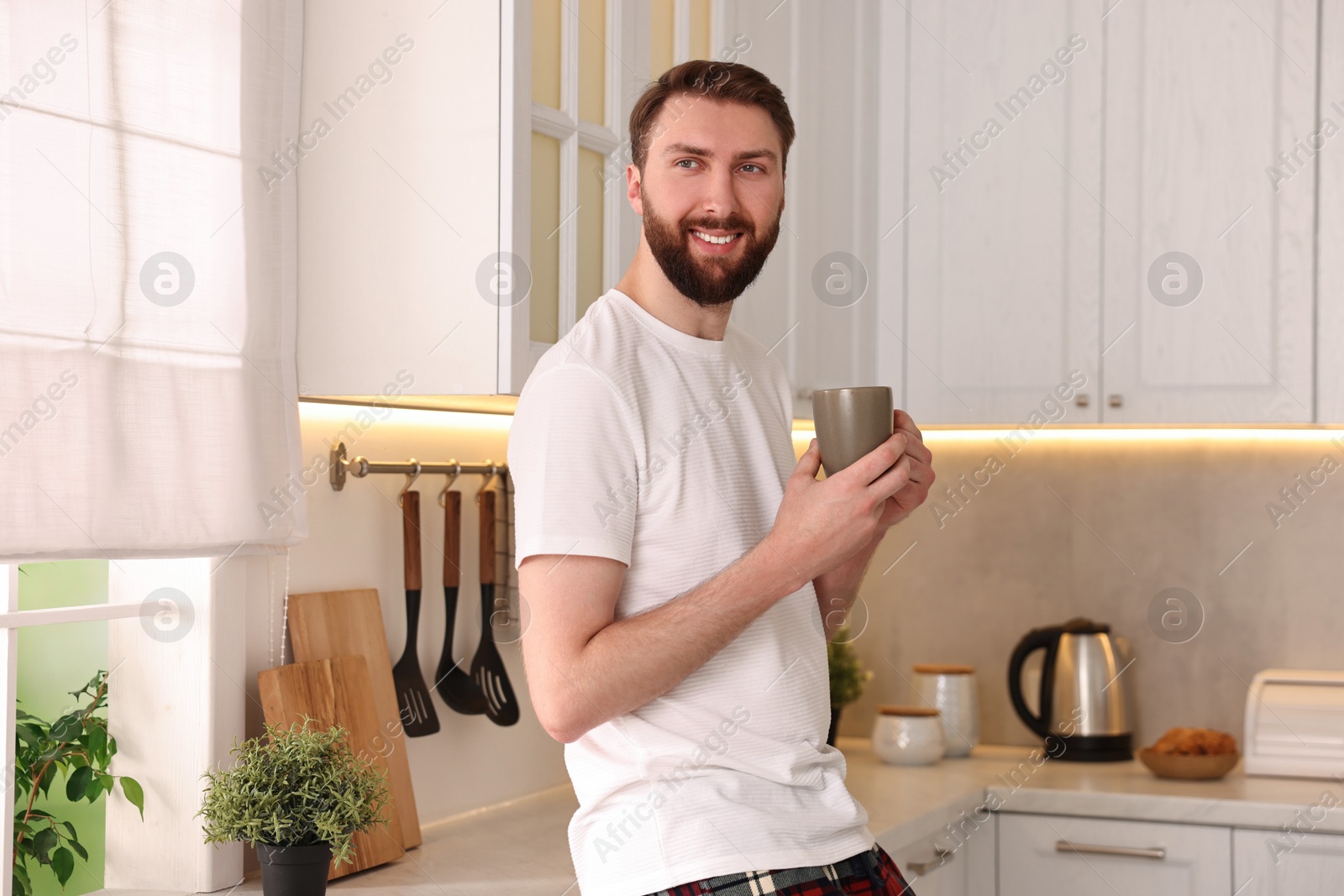 Photo of Happy young man with cup of coffee in kitchen at morning