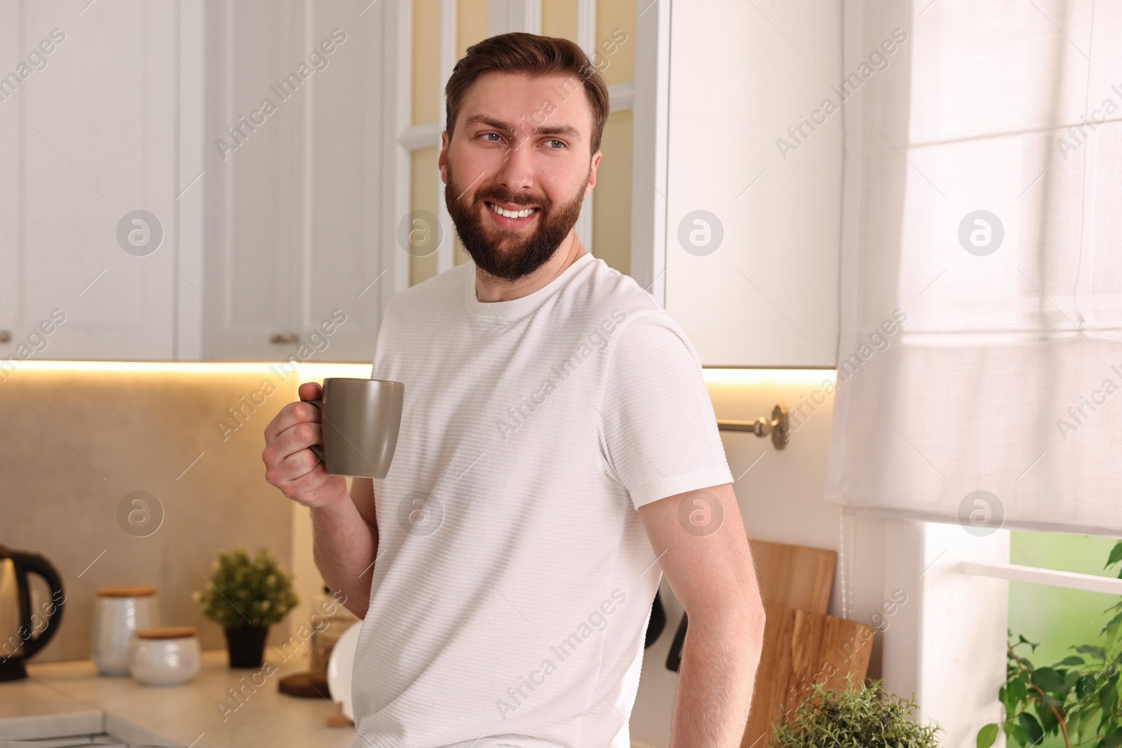 Photo of Happy young man with cup of coffee in kitchen at morning