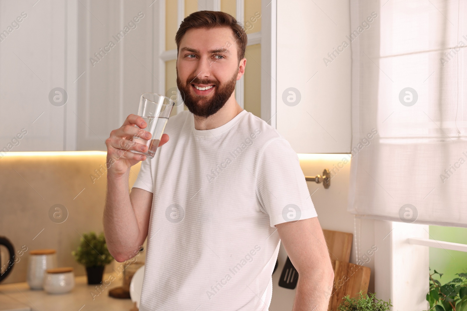 Photo of Happy young man with glass of water in kitchen at morning