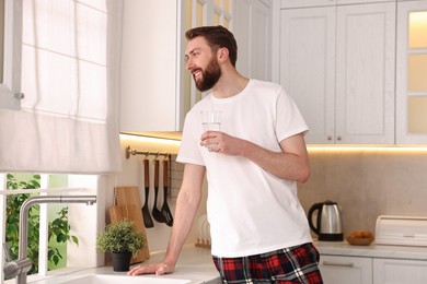 Photo of Happy young man with glass of water in kitchen at morning