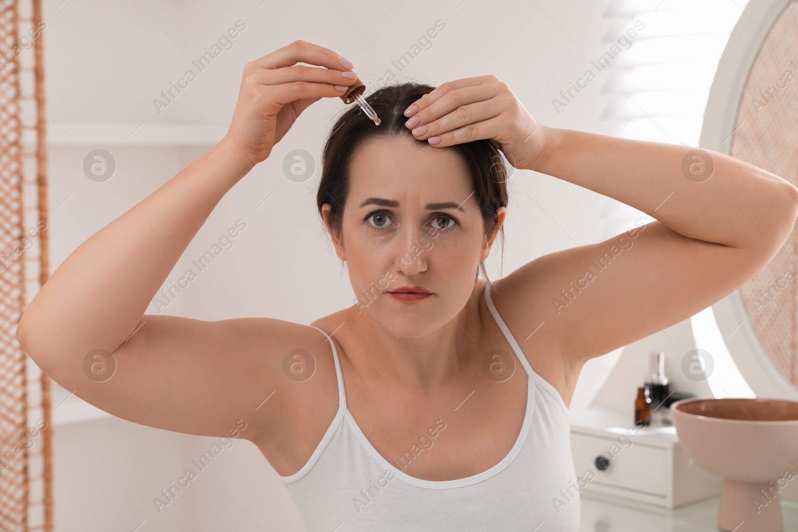 Photo of Hair loss problem. Woman applying serum onto hairline indoors