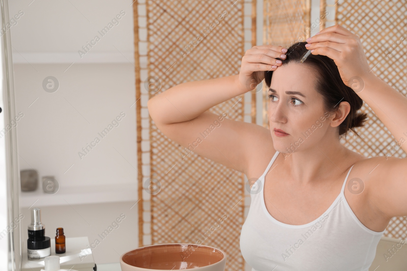 Photo of Hair loss problem. Woman applying serum onto hairline near mirror at home