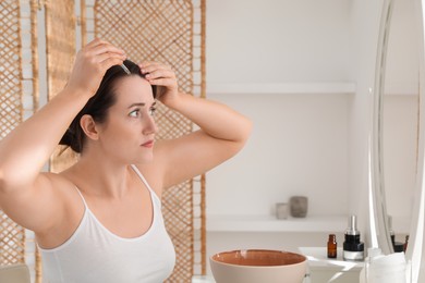 Photo of Hair loss problem. Woman applying serum onto hairline near mirror at home