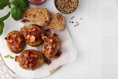 Photo of Delicious baked potatoes with bacon, bread and peppercorns on white tiled table, flat lay. Space for text