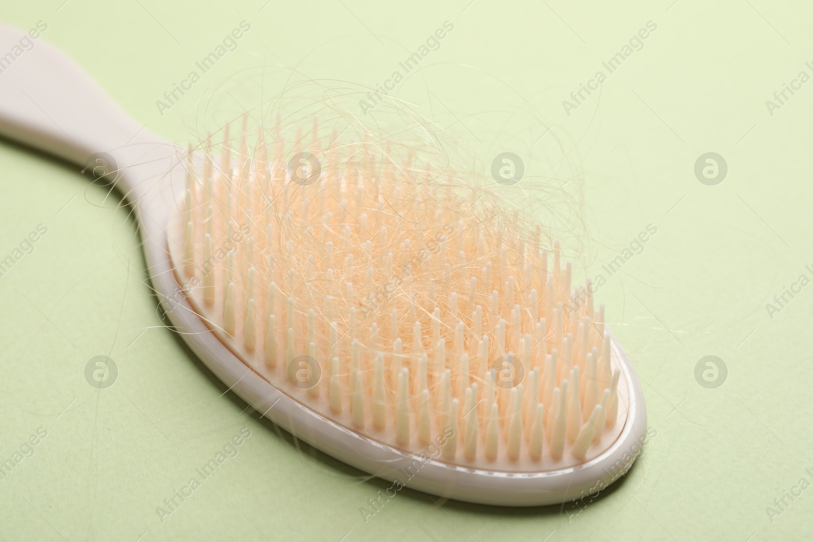 Photo of One brush with lost hair on light olive background, closeup. Alopecia problem