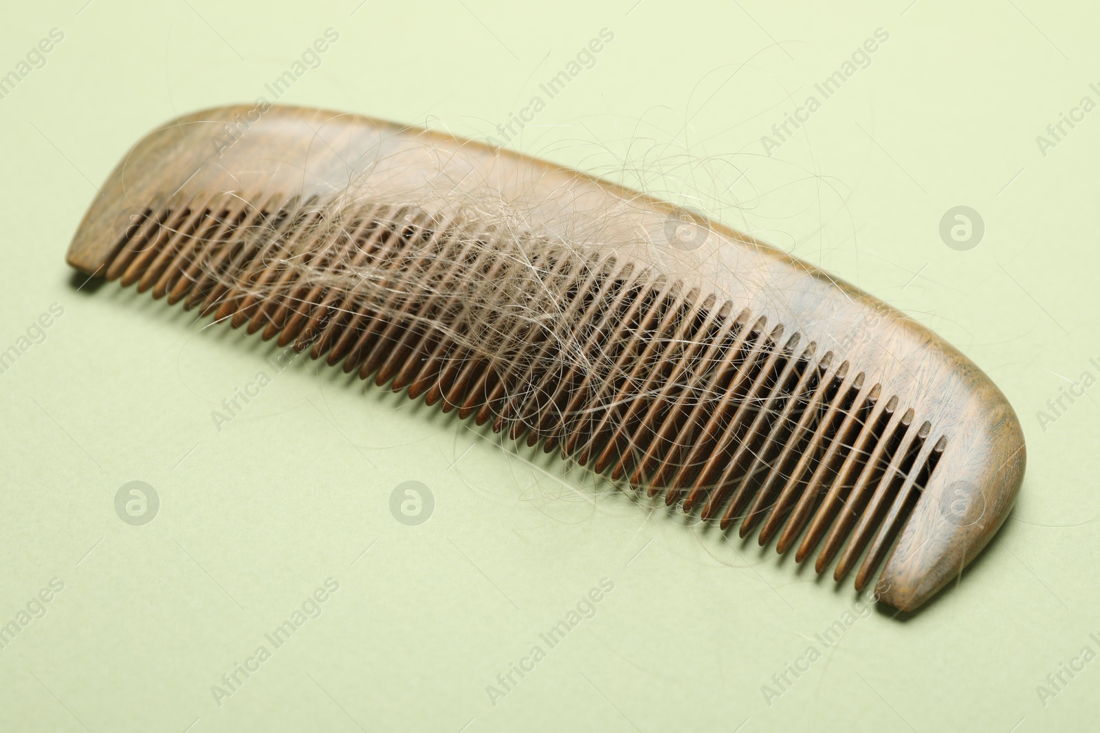 Photo of One comb with lost hair on light olive background, closeup