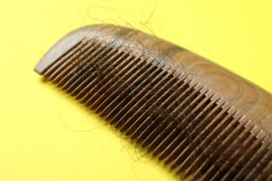 Photo of One comb with lost hair on yellow background, closeup. Alopecia problem