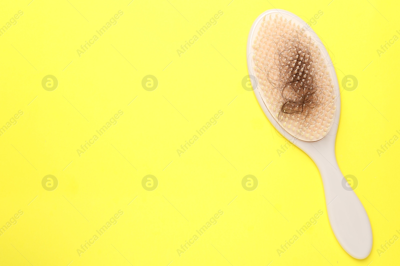 Photo of One brush with lost hair on yellow background, top view. Space for text