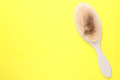 Photo of One brush with lost hair on yellow background, top view. Space for text