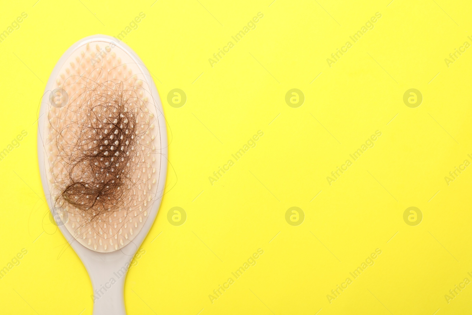 Photo of One brush with lost hair on yellow background, top view. Space for text