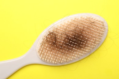 Photo of One brush with lost hair on yellow background, top view