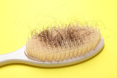 One brush with lost hair on yellow background, closeup. Alopecia problem