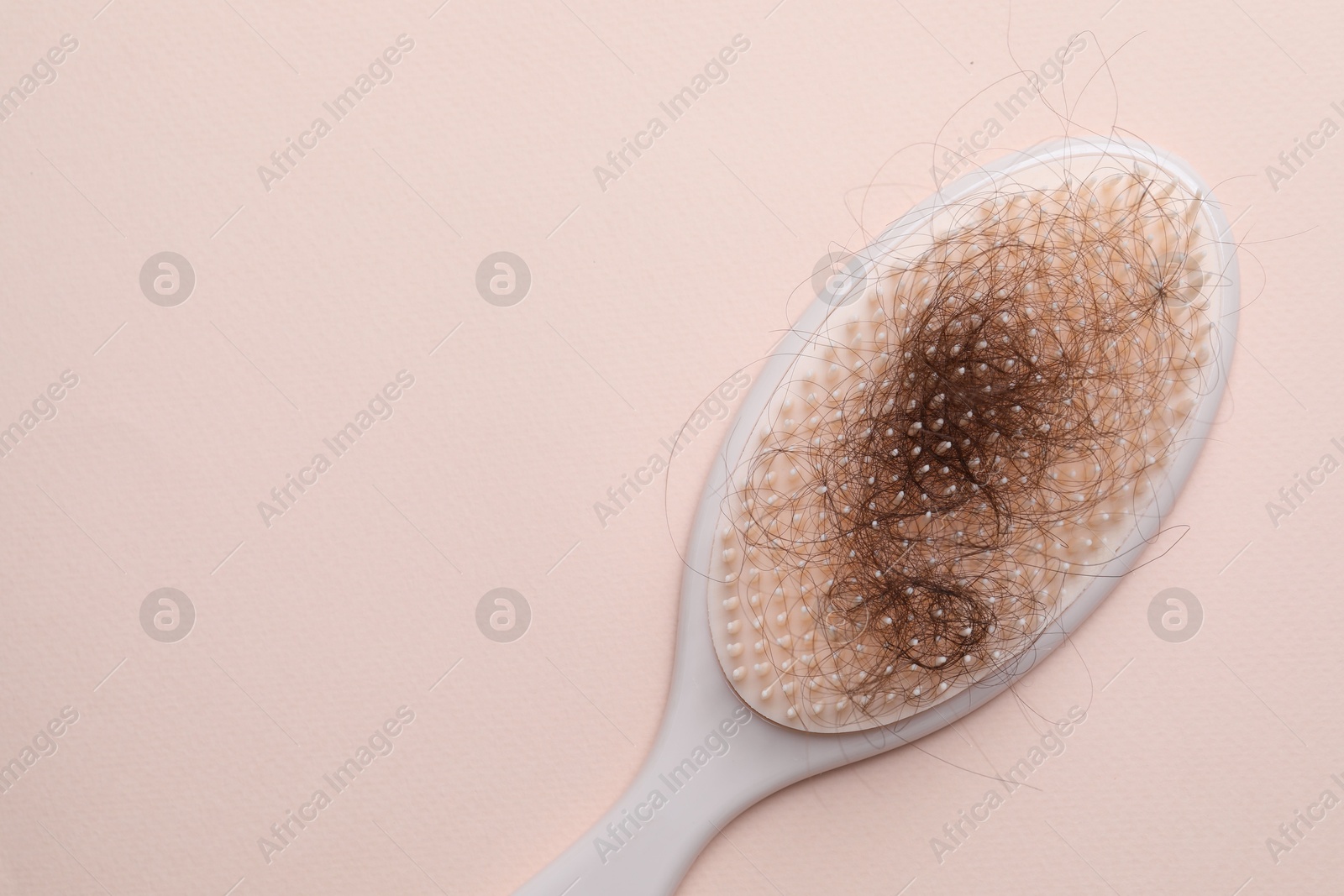 Photo of One brush with lost hair on light pink background, top view. Space for text