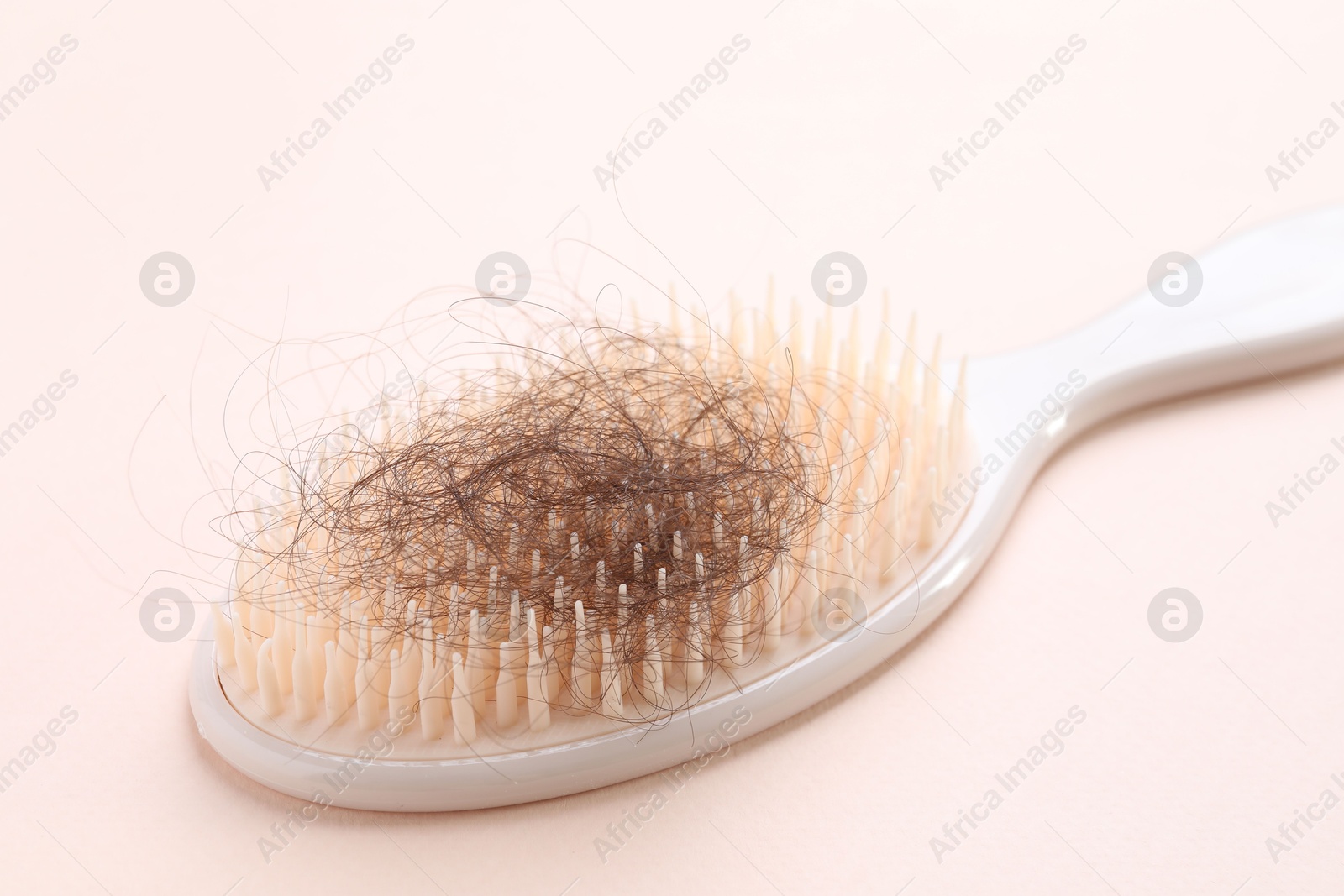 Photo of One brush with lost hair on light pink background, closeup. Alopecia problem