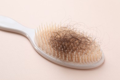 One brush with lost hair on light pink background, closeup. Alopecia problem