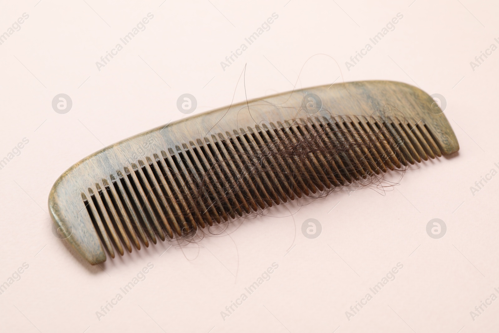 Photo of Comb with lost hair on light pink background. Alopecia problem