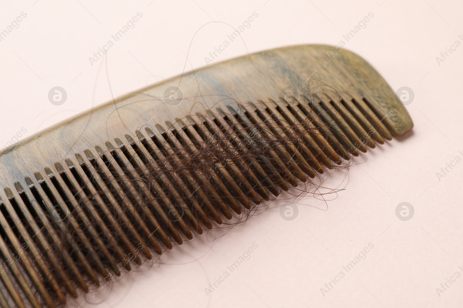 Photo of Comb with lost hair on light pink background, closeup. Alopecia problem