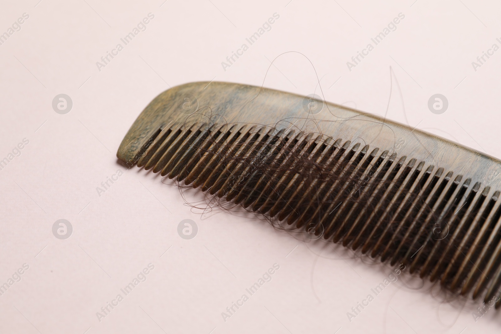 Photo of Comb with lost hair on light pink background. Alopecia problem