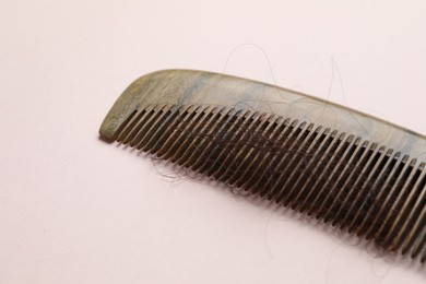 Comb with lost hair on light pink background. Alopecia problem