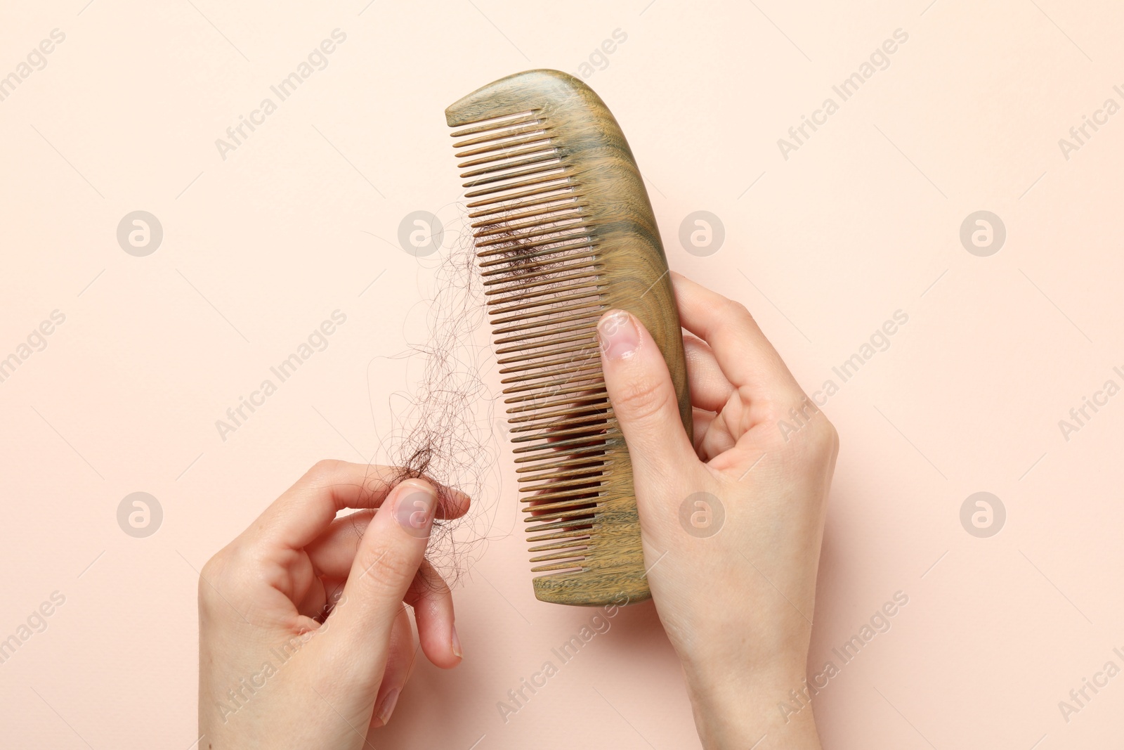 Photo of Woman taking her lost hair from comb on light pink background, top view. Alopecia problem