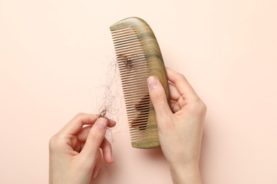 Woman taking her lost hair from comb on light pink background, top view. Alopecia problem