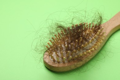 One brush with lost hair on light green background, closeup. Alopecia problem