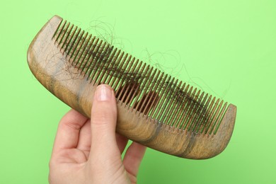 Woman with comb and lost hair on light green background, closeup. Alopecia problem