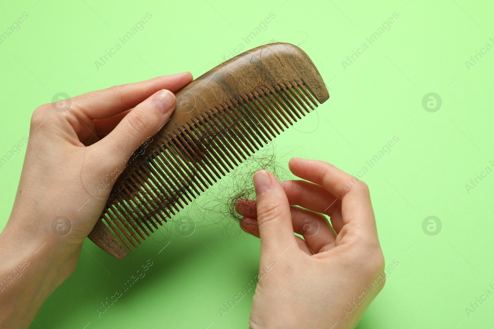 Photo of Woman taking her lost hair from comb on light green background, closeup. Alopecia problem