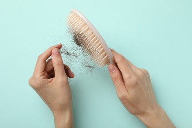 Photo of Woman taking her lost hair from brush on light blue background, top view. Alopecia problem