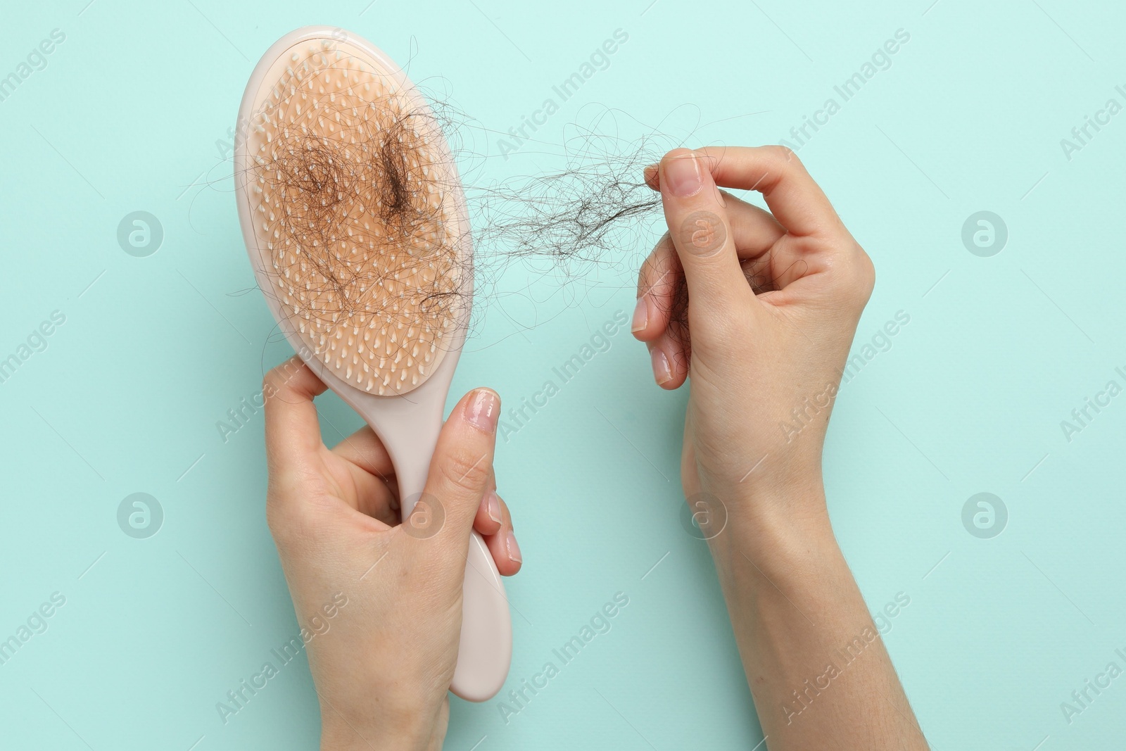 Photo of Woman taking her lost hair from brush on light blue background, top view. Alopecia problem