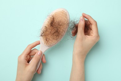 Photo of Woman taking her lost hair from brush on light blue background, top view. Alopecia problem