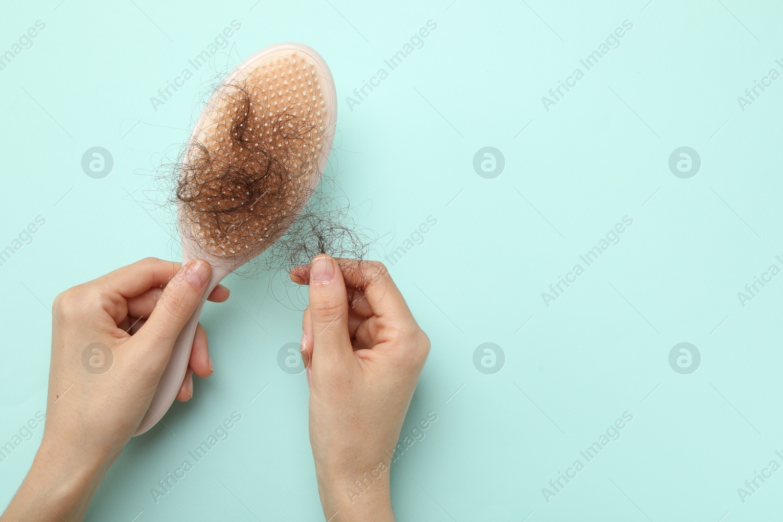 Photo of Woman taking her lost hair from brush on light blue background, top view. Space for text