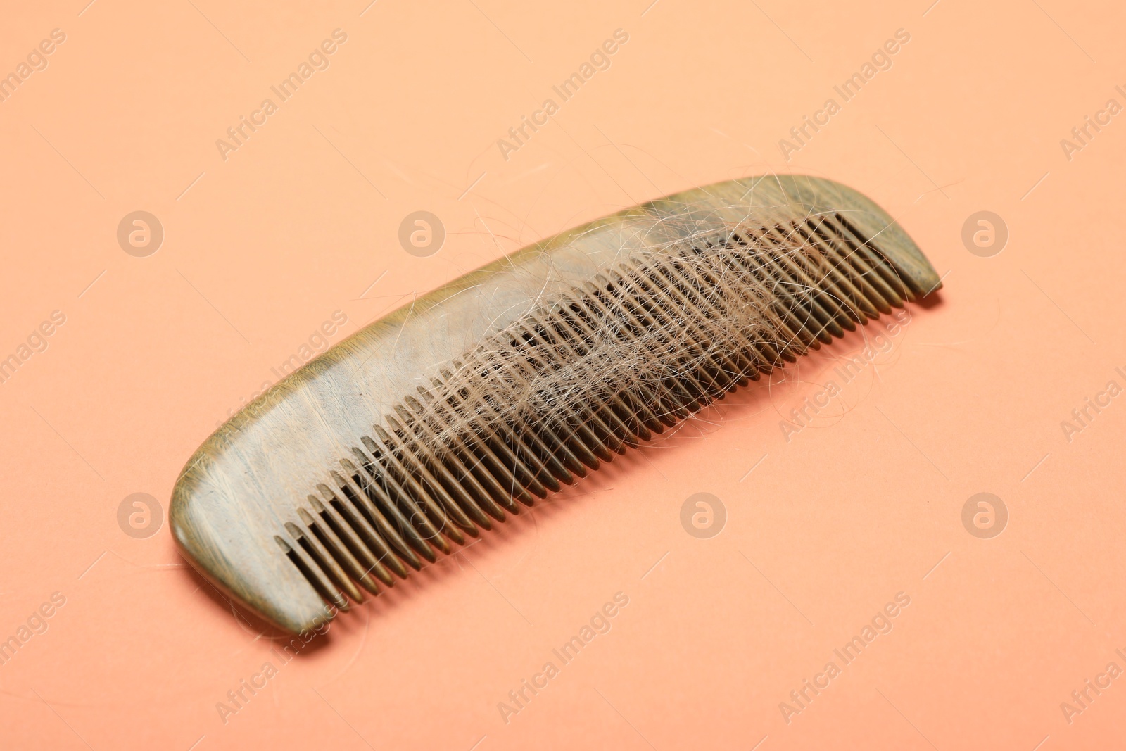 Photo of Comb with lost hair on coral background. Alopecia problem