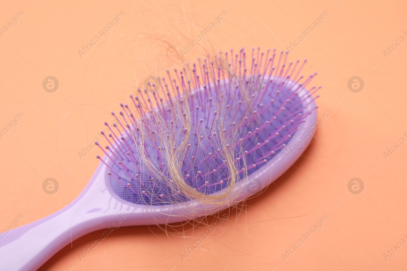 Photo of One brush with lost hair on coral background, closeup. Alopecia problem