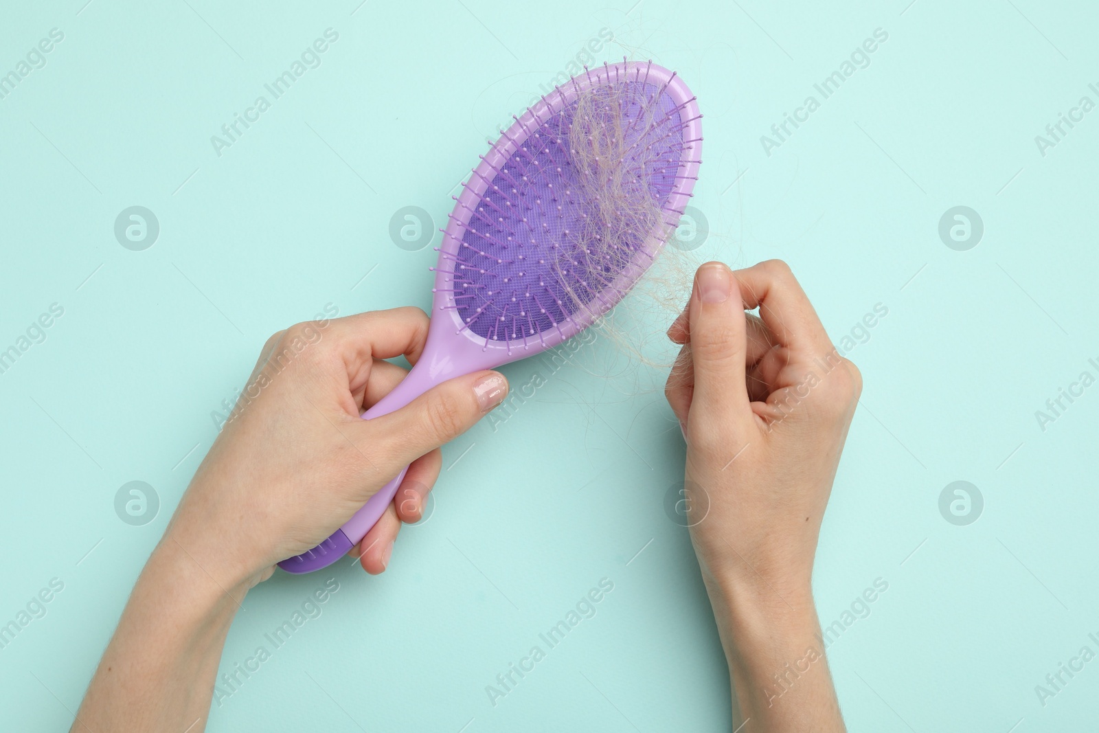 Photo of Woman taking her lost hair from brush on light blue background, top view. Alopecia problem