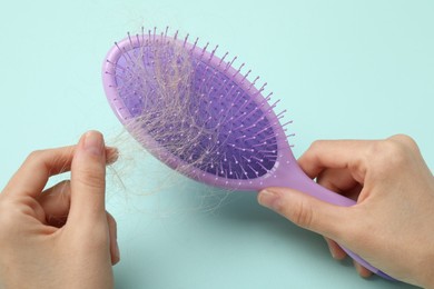 Woman taking her lost hair from brush on light blue background, closeup. Alopecia problem