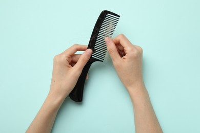 Woman taking her lost hair from comb on light blue background, top view. Alopecia problem