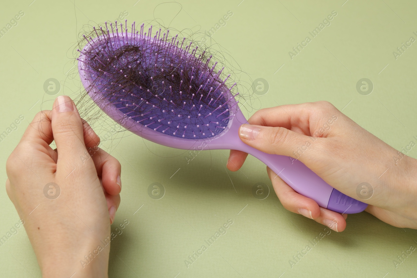 Photo of Woman taking her lost hair from brush on light olive background, closeup. Alopecia problem