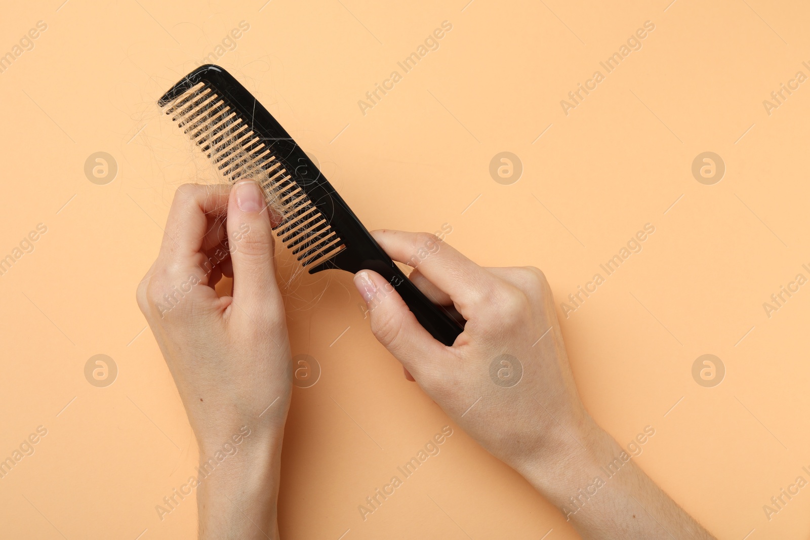 Photo of Woman taking her lost hair from comb on coral background, top view. Alopecia problem