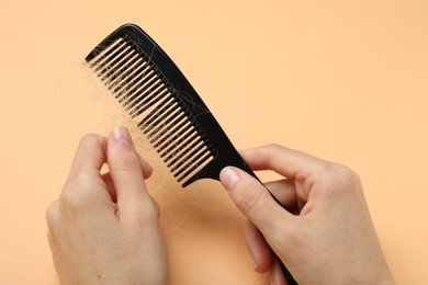 Woman taking her lost hair from comb on coral background, closeup. Alopecia problem