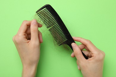 Woman taking her lost hair from comb on light green background, top view. Alopecia problem