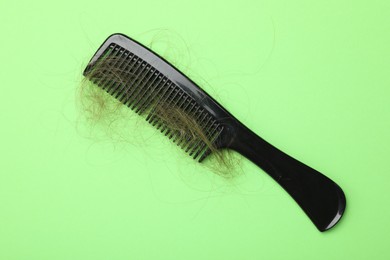 One comb with lost hair on light green background, top view. Alopecia problem