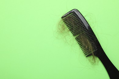 One comb with lost hair on light green background, top view. Space for text